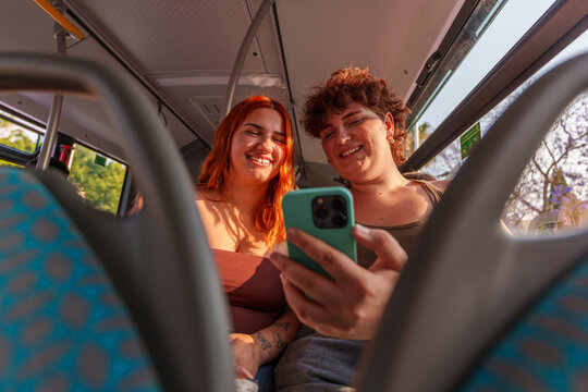 Two friends feeling joy and connection while looking at a cellphone on a city bus. Sharing a happy moment
