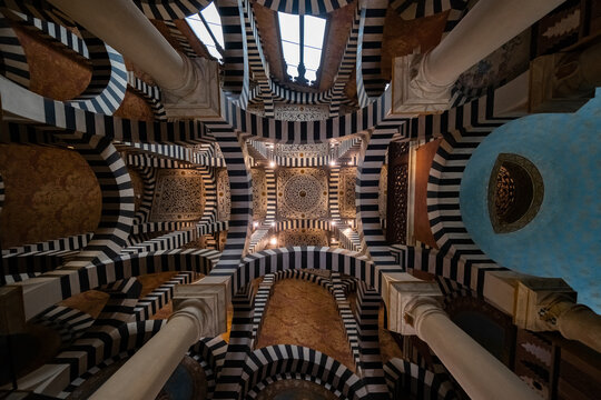 Bologna, Italy - 27 March 2022: View of the Palazzo della Mercanzia's ceiling, where striped arches converge towards an ornate central dome, framed by classical columns and soft, ambient light.