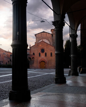 Bologna, Italy - 27 March 2022: View of the Basilica di San Francesco standing proudly against the soft, dusky sky, framed by the dark, imposing columns of a portico.