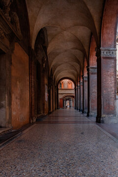 Bologna, Italy - 27 March 2022: View of the ancient porticoes casting long shadows with a mosaic floor leading the eye to a distant light.