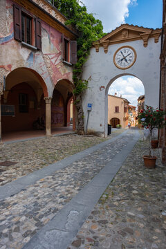 Bologna, Italy - 26 March 2022: View of the ancient archway clock tower and weathered buildings, where pastel hues meet the rough, textured stone under a bright sky.