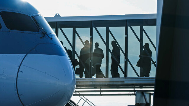 Silhouette of passengers walking through a glass jet bridge to board a large modern airplane at the airport