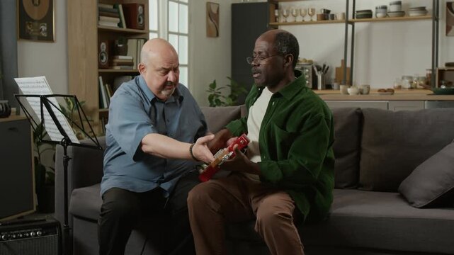 Front view shot of middle aged male music teacher talking to frustrated senior man learning to play electric guitar in studio, copy space Suitable for challenges in learning campaigns or education ads