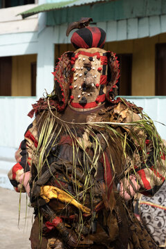 Ganvie, Benin - 14 April 2023: View of a figure adorned in a vibrant, textured costume, with intricate details and earthy tones, standing out against a building backdrop.