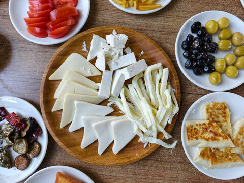 Various cheeses and accompaniments arranged on a wooden platter with side dishes present at a meal