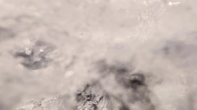 Close to surface over bubbling water flow under waterfall, slow motion. Extreme close-up detail of splashing and foaming water in mountain river stream