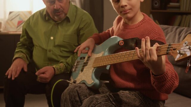Cinematic close up shot of child playing electric guitar male music teacher or grandfather cheering in background Ideal for promotional visuals for kids programs