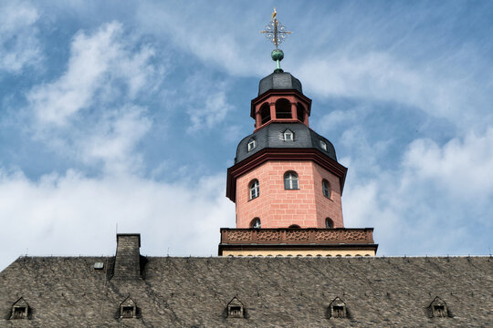 Frankfurt am Main, Germany - 10 April 2017: View of a historic reddish-pink tower, its dark spire piercing the vivid blue sky, rising above a textured grey roof.