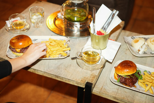Young woman eating gourmet hamburger inside pub bar while drinking hot tea - Food, real people lifestyle and trends concept - UGC flash content - Main focus on right burger