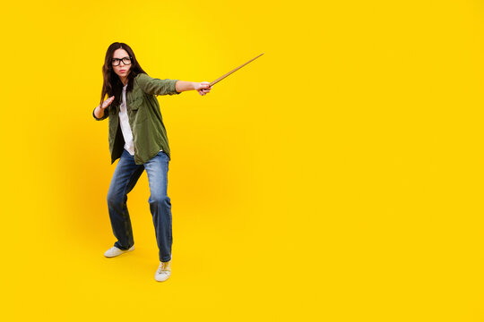 Young woman in glasses striking a dynamic wizard pose with a wand on a vibrant yellow background, playful magic cosplay and confident full-length portrait conveying power and energy
