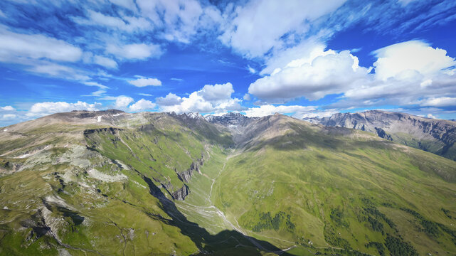 Aerial view of majestic green slopes and rugged peaks of the Hohe Tauern range under a brilliant blue sky, Nationalpark Hohe Tauern, Carinthia, Austria.