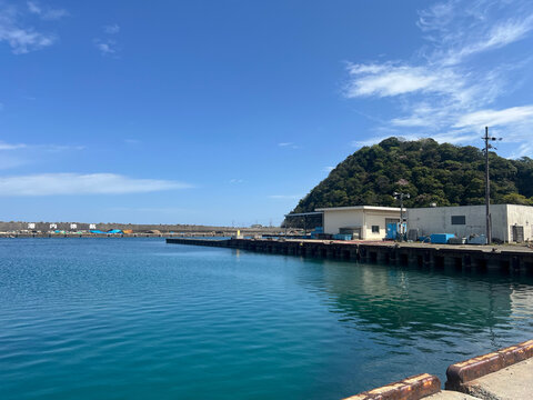 漁港の岸壁と青い海と緑の小山