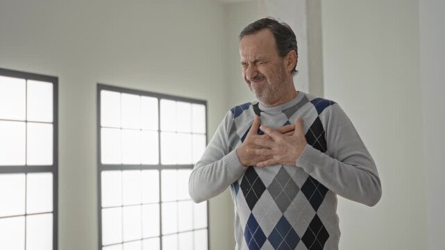 Man clutch chest with hand pressed to heart, grimace signaling arrest in building; pain emergency.