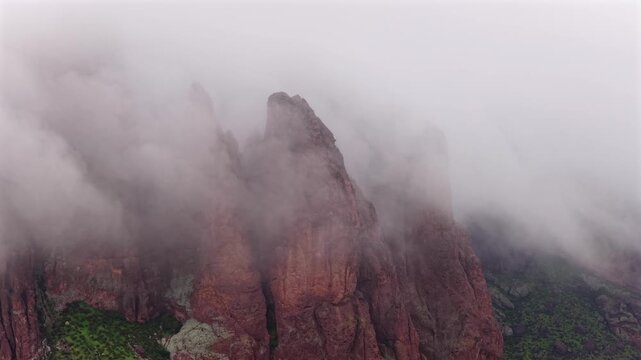 Aerial view of majestic, reddish-brown rock formations shrouded in thick, ethereal mist, contrasting with vibrant green, Apache Junction, Arizona, United States.