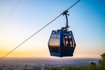 Blue cable car gondola suspended on wire against orange sunset sky © Ployker