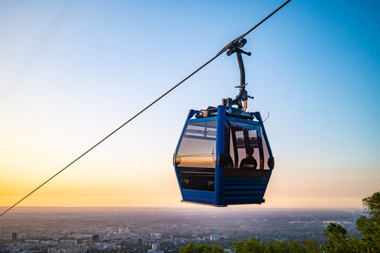 Blue cable car gondola suspended on wire against orange sunset sky
