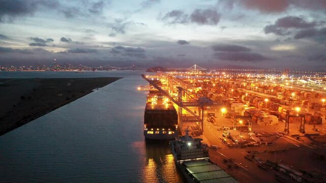 Oakland, United States - 15 September 2025: Aerial view of the bustling Port of Oakland, glowing with golden lights, contrasting with dark bay waters and the distant San Francisco skyline.