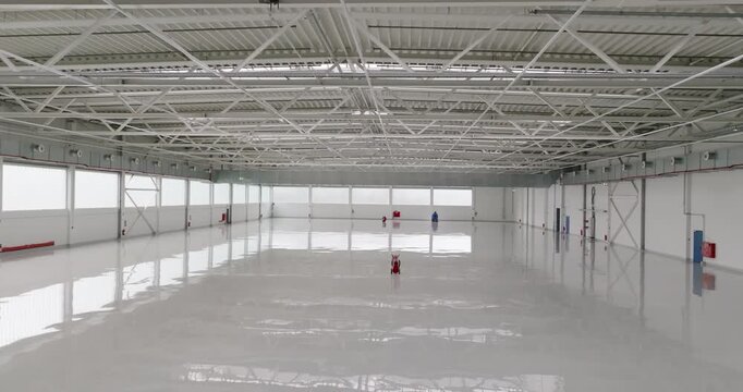 Wide angle interior shot of a vast empty industrial warehouse with high ceiling and white walls