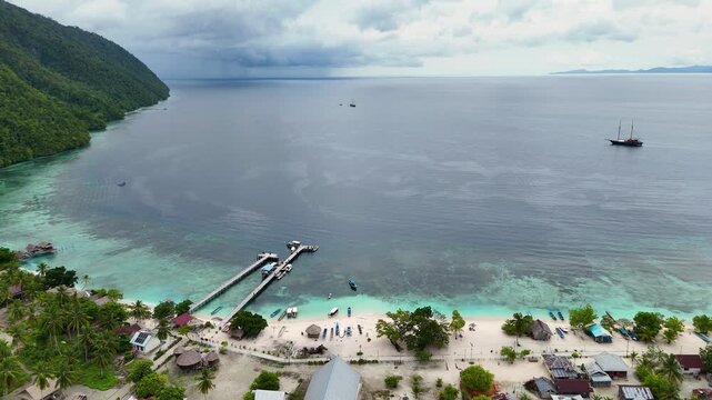 Aerial view of a long wooden pier reaching into vibrant turquoise waters, contrasting with a lush green island and distant dark clouds, Sauwanderek, West Papua, Indonesia.