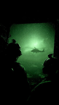 Scena militare notturna vista attraverso visori notturni, elicottero nero che sorvola truppe a terra, effetto grainy verde intenso, luce fioca, misteriosa e tesa, verticale
