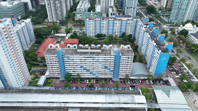 Aerial view of vibrant light blue and white HDB flats amidst lush greenery and bustling roads, showcasing a dense urban tapestry under a cloudy sky, Singapore, Singapore, Singapore.