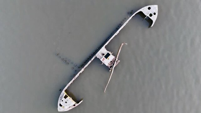 Aerial view of a ghostly shipwreck resting in murky, dull grey-green waters, offering a stark contrast against its pale, decaying hull, Nyack, New York, United States.
