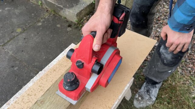 An electric planer cutting a board. A close-up top view. A craftsman using an electric planer. Interior renovation. Interior restoration and refurbishment. Home improvement.