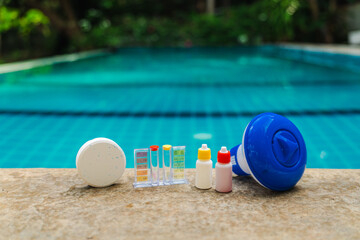Obraz premium Pool maintenance tools lined on pool edge with chlorine tablet, water test kit, reagent bottles and floating dispenser