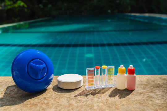 Pool maintenance tools including chlorine dispenser, tablet, water testing kit, and reagent bottles on pool edge for swimming pool care, chemical balance, and water quality control
