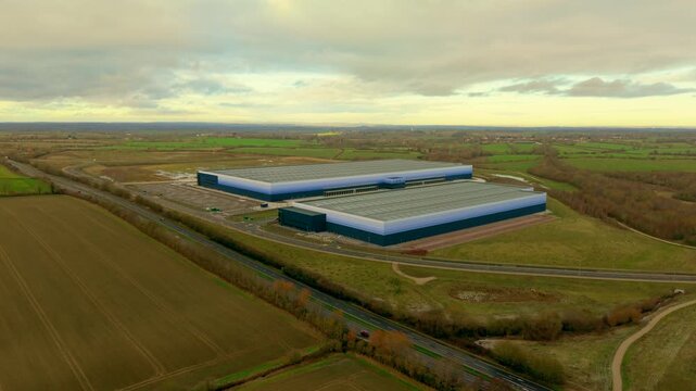 Expanding warehouse complexes operating logistics workflows across industrial countryside. Large distribution facilities managing storage transportation supply chain operations. Modern production hubs