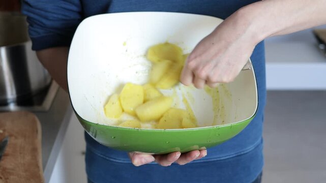 Person tossing seasoned potato wedges in a green bowl with a fork