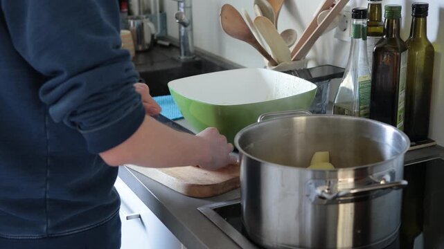 Person preparing food in a kitchen, cooking potatoes in a pot