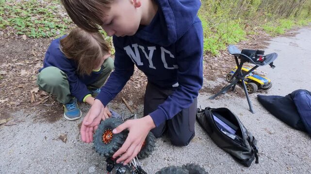 Two boys repairing a remote control RC crawler car on a forest road, close up