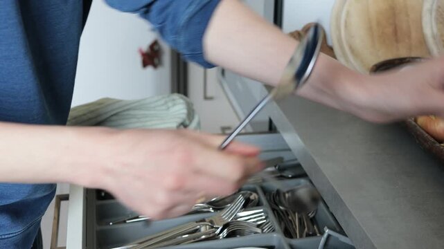 Person organizing kitchen cutlery drawer with spoons, forks, and knives
