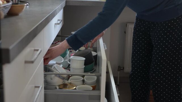 Person organizing kitchen cabinets, putting away dishes and cups neatly