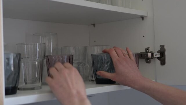 Hand organizing glassware on a kitchen cabinet shelf