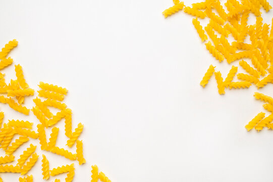 Dry uncooked Italian pasta scattered on white background, top view space for text. Spiral pasta, fusilli. Food background, organic macaroni made from wheat flour