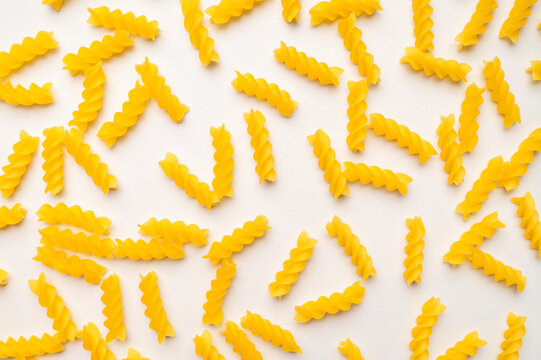 Dry uncooked Italian pasta scattered on white background, top view. Spiral pasta, fusilli. Food background, organic macaroni made from wheat flour