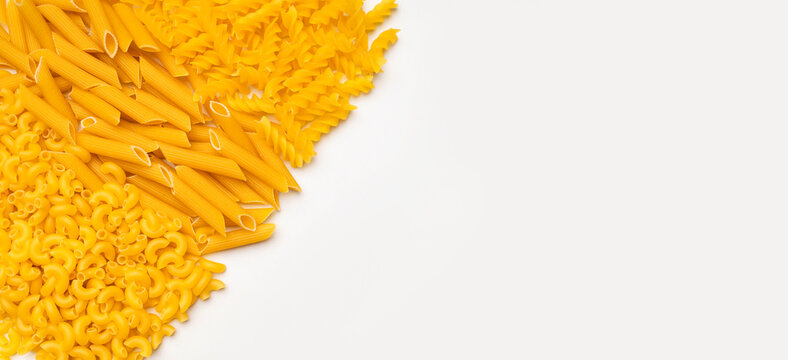 Dry uncooked Italian pasta scattered on white background, top view space for text. Spiral pasta, fusilli, penne, spaghetti. Food background, organic macaroni made from wheat flour