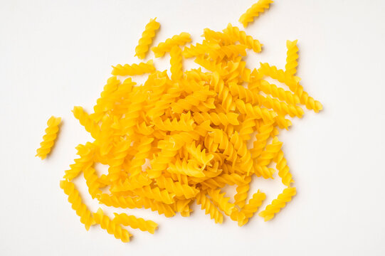 Dry uncooked Italian pasta scattered on white background, top view space for text. Spiral pasta, fusilli. Food background, organic macaroni made from wheat flour