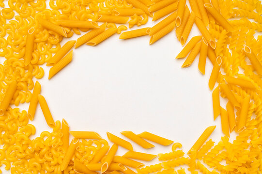 Dry uncooked Italian pasta scattered on white background, top view space for text. Spiral pasta, fusilli, penne, spaghetti. Food background, organic macaroni made from wheat flour