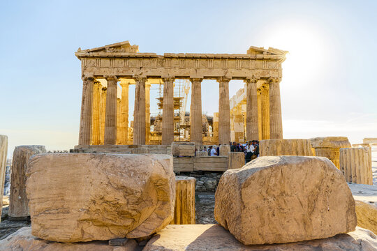 View of the majestic, sun-drenched Parthenon with its grand columns and scaffolding, rising above rugged ancient stone blocks, Athens, Central Athens Regional Unit, Greece.