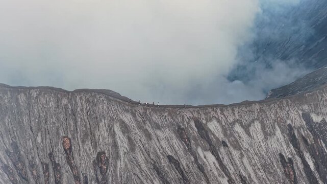 People trekking along the smoking active volcano crater rim of mount bromo in indonesia