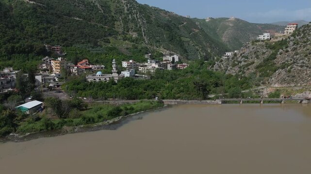 Wide drone view of Oyoun El Samak reservoir in Akkar with natural mountain landscape and visitors crossing the dam bridge
