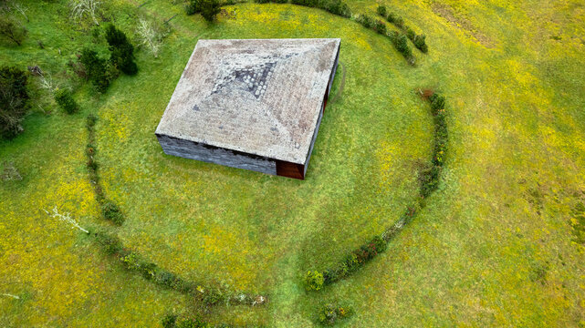 Aerial view of a solitary square structure amidst a verdant field, encircled by a quaint hedge, creating a striking contrast of geometric precision and natural curves, Ponta Delgada, Azores, Portugal.