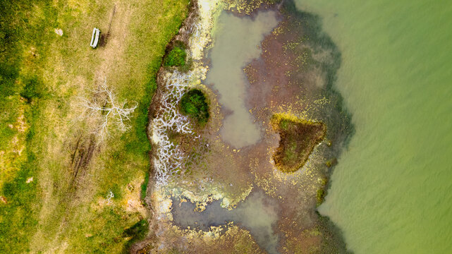 Aerial view of green land meeting an earthy marsh and emerald water, with a boat on the shore, Ponta Delgada, Azores, Portugal.