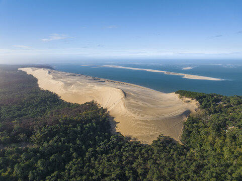 Aerial view of a vast golden sand dune sharply dividing lush green forest from the tranquil blue bay, La Teste de Buch, Nouvelle-Aquitaine, France.