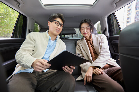 A businessman and businesswoman converse in the back seats of a car