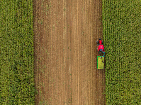 Aerial view of a vibrant red tractor meticulously harvesting a field, creating a striking contrast between the rich brown soil and the lush green crops, Tuzla, Bosnia and Herzegovina.