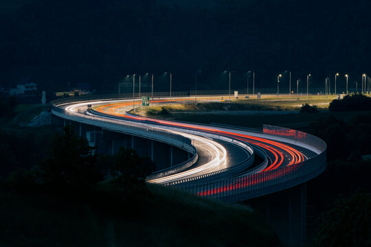 Aerial view of a winding highway bridge at night, adorned with vibrant light trails from passing vehicles, contrasting against the deep dark sky, Tuzla, Bosnia and Herzegovina.